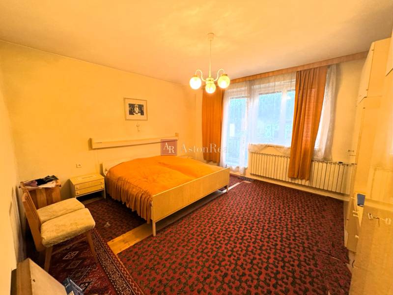 Spálňa v rodinnom dome s kobercovou podlahou, veľkým oknom a starším nábytkom.